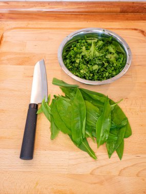 Mutfak tahtasının üzerinde taze sarımsak kokulu Ramson yaprakları doğramak. Bahar bitkisel besin bileşenleriyle sağlıklı yemek..