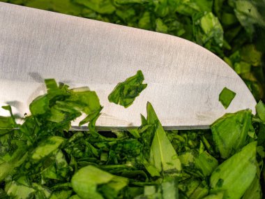 Taze doğranmış Ramson yaprakları ya da krom kasede yabani ayı sarımsak yaprakları. Ahşap masa, soğuk paslanmaz çelik bıçak ve mutfakta yabani sarımsak yaprakları. Üst görünüm. 