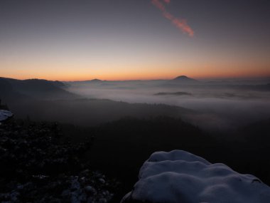 Soğuk bir sabah, kayalık kenarda kar, renkli bir sis vadisi. Kış tepe manzarası 
