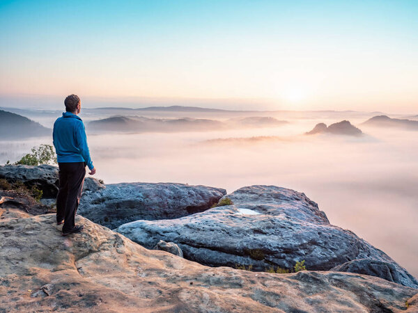 Hiker watch misty melancholic morning in cloudscape. View into long deep valley full of fresh spring mist. Landscape within daybreak after rainy night 