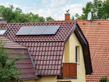 Aile evinin fayanslı çatısındaki elektrikli güneş panelleri. Evin yalıtılmış cephesi enerji yoğunluğunu azaltıyor..