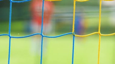 Futbol kapısı ağından bak. Kaleci, rakiplerin saldırısı sırasında yavaşça geri çekiliyor. Soyut görüş. Yavaş çekim.