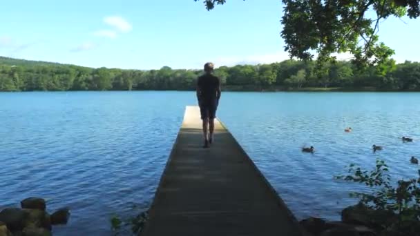 十几岁的男孩走在木制码头的尽头 坐在湖面上放松 — 图库视频影像