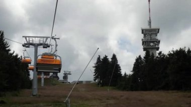 Yazın kayak merkezinin yukarısındaki teleferik kulübeleri. Klinovec tepesi, ormanda vericisi olan kule. Yavaş çekim