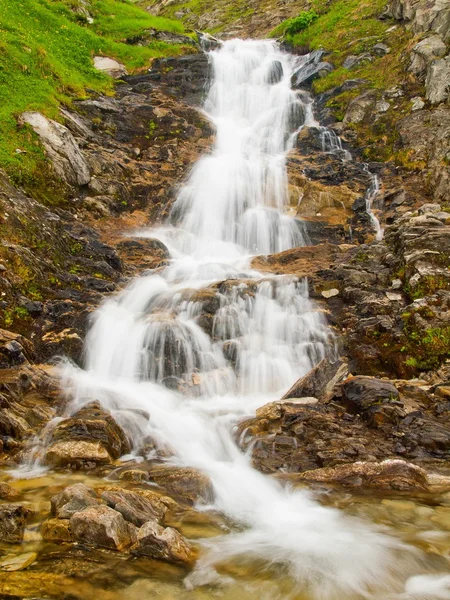 Piccolo ruscello veloce nel fresco prato verde delle Alpi, cime innevate delle Alpi sullo sfondo. Freddo nebbia e pioggia in montagna alla fine dell'estate . — Foto Stock