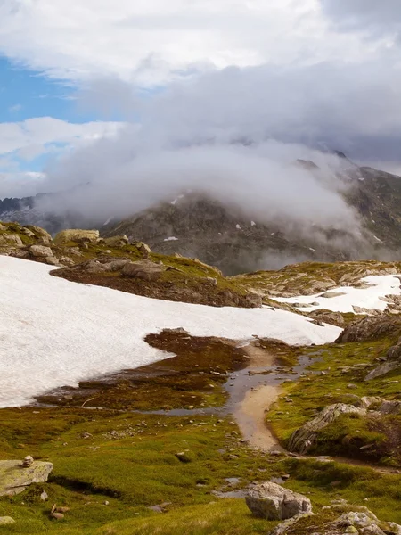 Stony snowy autumn meadows of high Alpine mountains. Dark peaks touch heavy misty clouds. Cold and damp end of the day in Alps mountains — Stock Photo, Image