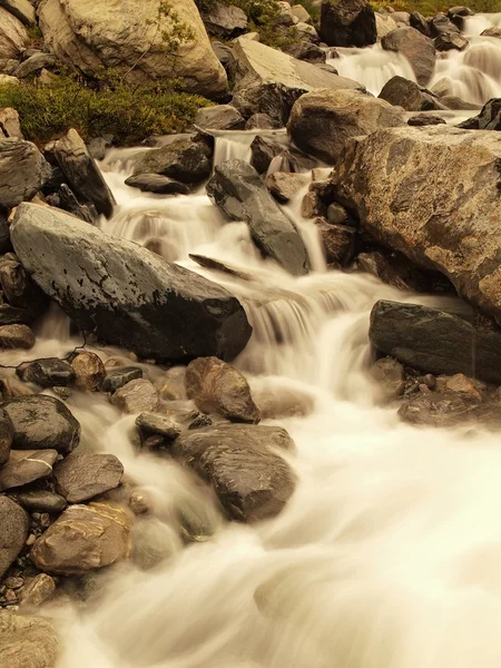 Pericolo torrente allagato in rapida corsa sulle rocce. Onde sfocate di fiume alpino che scorrono su massi e sassi, bolle nell'acqua  . — Foto Stock