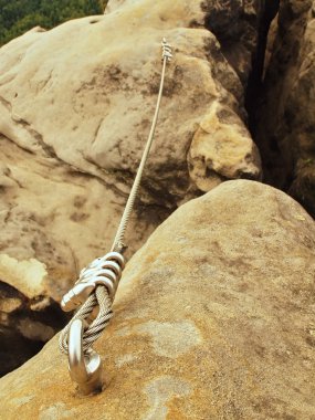 Detail of thin iron rope end anchored for climbers into sandstone rock. Iron twisted rope fixed with srew clamps in block. Safety footpath between rocks. clipart