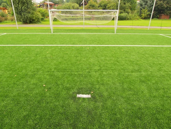 Detalhe de um ponto de penalidade em fron de campo goleiro. Campo de jogos de futebol vista de campo de grama artificial, portão no final. Grama de plástico e borracha preta finamente moída . — Fotografia de Stock