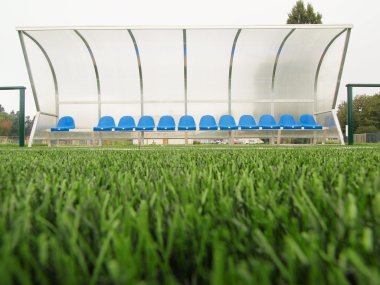 Yeni mavi plastik koltuk açık stadyum oyuncular bankta sandalye şeffaf plastik çatı altında yeni boya ile. plastik futbol yeşil çim Bahçesi.