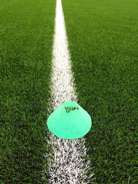 Leuchtend grünblauer Plastikkegel auf lackierter weißer Linie. Kunststoff Fußball grün Rasen Spielplatz mit schleifen schwarzem Gummi im Kern. — Stockfoto