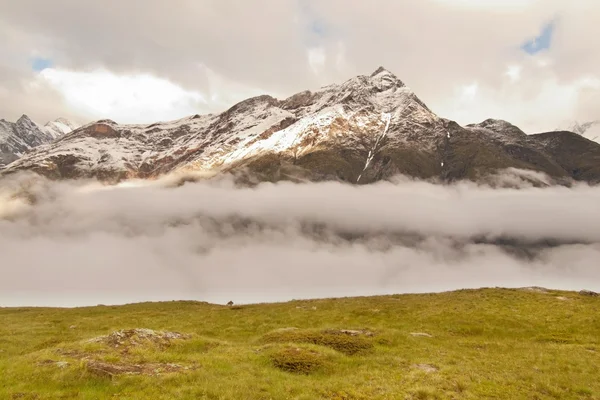 Scharfe schneebedeckte Gipfel der Alpenberge über dem Tal voller dichter Nebel — Stockfoto