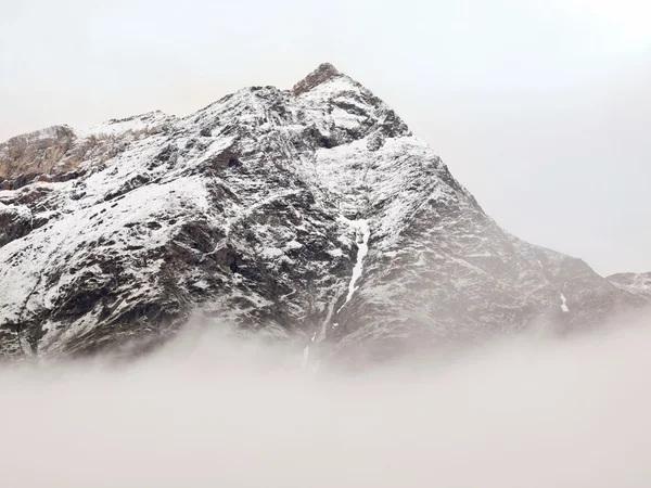 Picos nevados afiados de montanhas dos Alpes acima do vale cheio de nevoeiro pesado — Fotografia de Stock