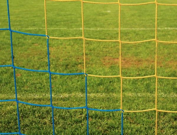 Detail překřížené modré žluté řetězec fotbal sítí. Trávě fotbalového hřiště v pozadí. — Stock fotografie