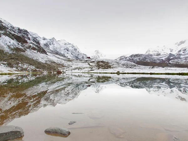 First snow in mountains. Autumn lake in Alps with mirror level. Misty sharp peaks of  high mountains in background. — Stock Photo, Image
