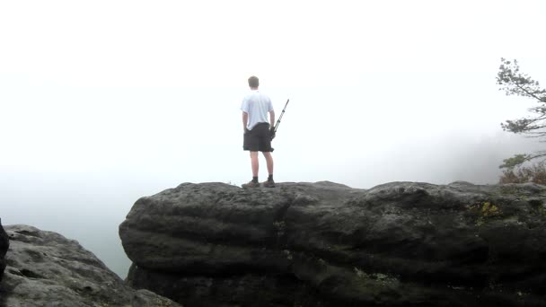 Fotografo con treppiede in piedi su un punto di vista roccioso e scattare foto di nebbioso paesaggio mattutino. Parco nazionale della Svizzera sassone in Germania. Malinconica mattina d'autunno . — Video Stock