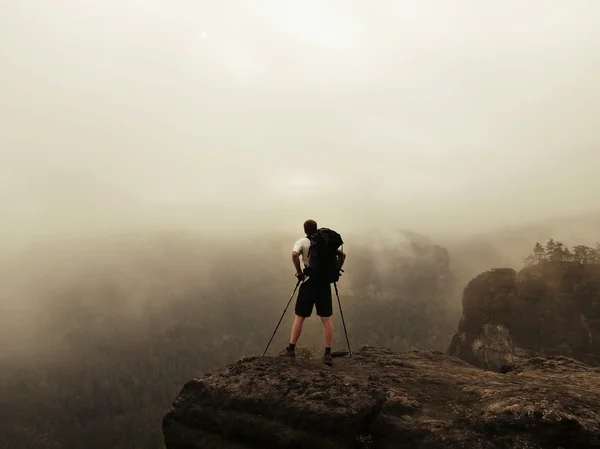 Turista con pali e grande zaino in piedi sul punto di vista roccioso e guardando in nebbioso paesaggio mattutino. Parco nazionale della Svizzera sassone in Germania. Malinconica mattina d'autunno . — Foto Stock