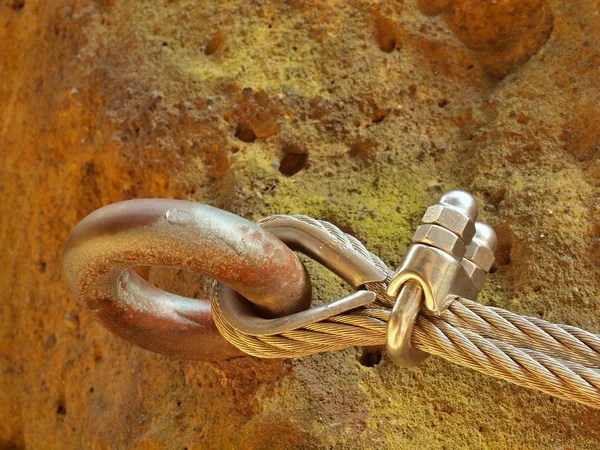 Detail of rope end anchored into sandstone rock. Iron twisted rope fixed in block by screws snap hooks. — Stock Photo, Image