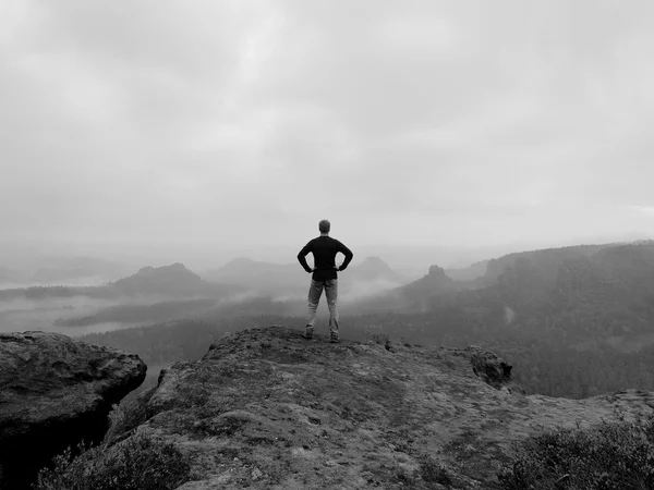 Tourist is standing on the peak of sandstone rock in rocky park and watching over the morning misty valley to big Sun. Black and white photo. — Stock Photo, Image