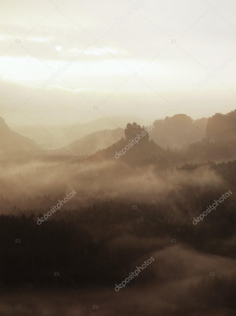 Autumn melancholic morning in rocky park. View into long deep valley full of heavy colorful mist. Autumn landscape within daybreak after rainy night