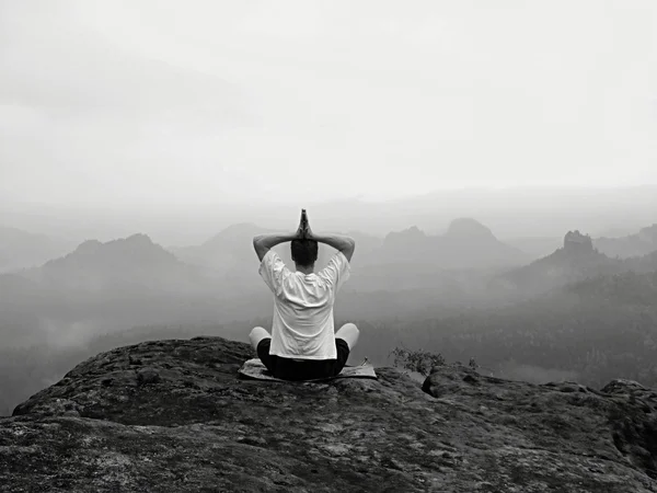 L'uomo sta facendo posa Yoga sulle rocce picco entro la mattina nebbiosa — Foto Stock