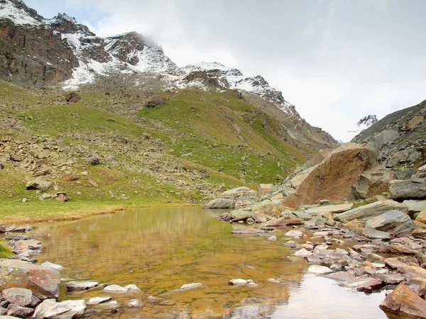 Höstens alpine lake med spegel. Steniga bergen ovanför sjön banker och skarpa snöiga och dimmiga toppar av höga berg. Mörka molnig himmel. — Stockfoto