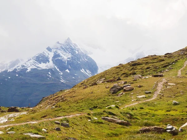 Stony groene heuvel blaten besneeuwde toppen van de Alpen. Scherpe Alpen bergen in de achtergrond steken in donkere zware hemel. Herfst begint. — Stockfoto