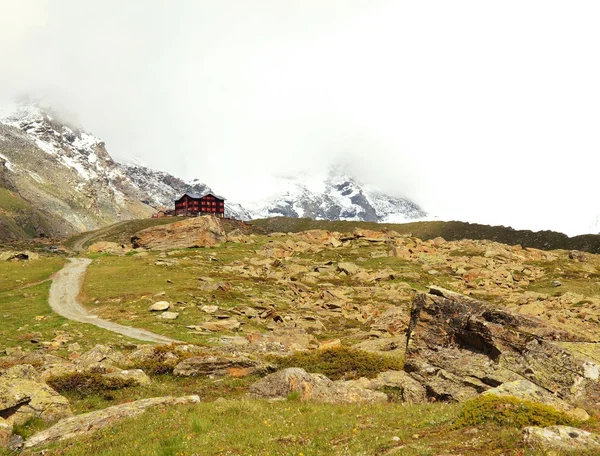 Piedra verde colina abajo nevado Picos alpinos. Alpes agudos montañas en el fondo que se adhieren en el cielo oscuro pesado. El otoño está empezando. . — Foto de Stock