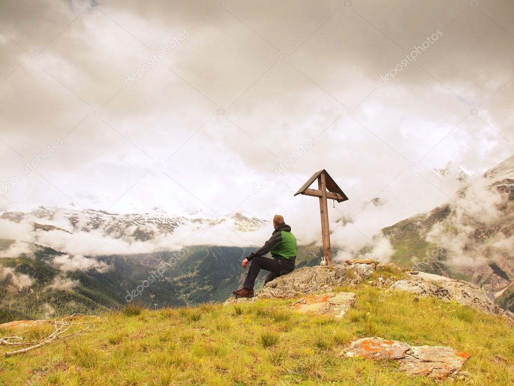 Tourist stand on rocky view point and watching into misty Alpine valley. Wooden cross at a mountain peak. Cross on top of a mountain peak as typical in the Alps.