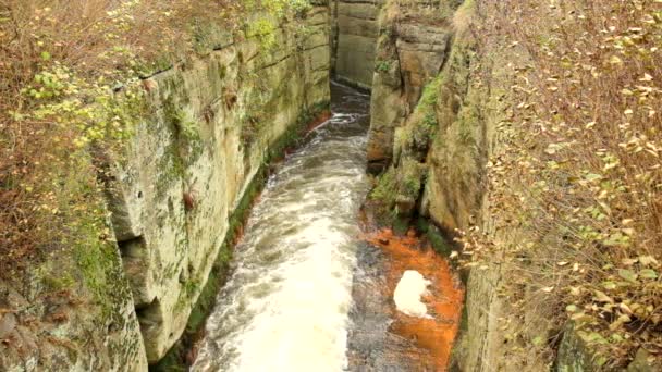 Fast full-flowing foamy water between sandstone rocks, orange sediments on dirty bank. Deep riverbed hewed into sandstone block — Stock Video