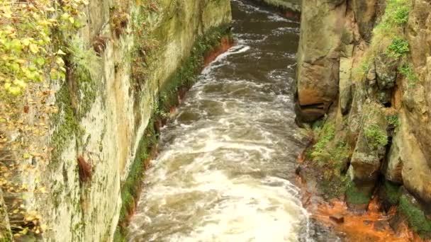 Fast full-flowing foamy water between sandstone rocks, orange sediments on dirty bank. Deep riverbed hewed into sandstone block — Stock Video