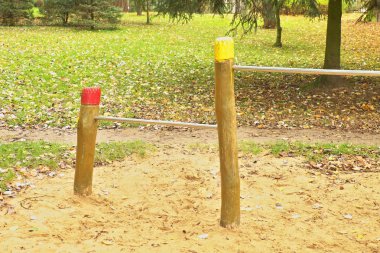 Çelik yatay çubuklar üzerinde ahşap sütunlar içinde çocuk oyun alanı. Turuncu kum barlar, yeşil park arka plan aşağıda.