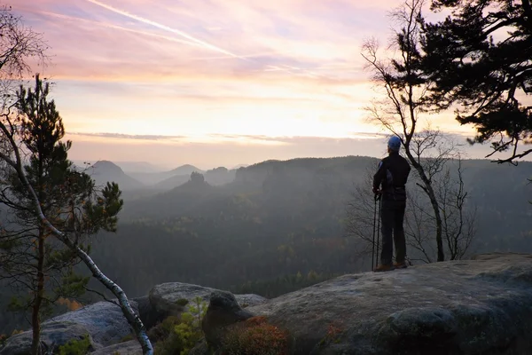 Turista com pólos está de pé no ponto de vista rochoso e assistindo em paisagem manhã nebulosa. Parque nacional do império do rock, manhã melancólica do outono . — Fotografia de Stock