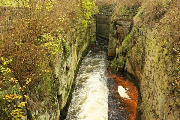 Schuimend volledig stromend water tussen zandsteenrotsen, oranje sedimenten op vuile bank. Diepe rivierbedding hakte in zandsteen blok — Stockfoto