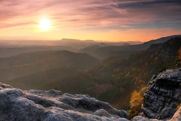 Sunset in a beautiful rocky park Bohemian-Saxony Switzerland. Sandstone peaks and hills increased from foggy background, the fog is orange due to sun rays. — Stock Photo, Image