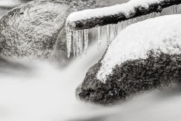 Rokerige koud water van bergbeek in de winter. Lange crystal ijspegels zijn opknoping boven melkachtig water niveau. Grote granieten keien. — Stockfoto