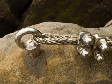 Detail of rope end of ferrata way anchored into sandstone rock. Iron twisted rope fixed in block by screws snap hooks. clipart