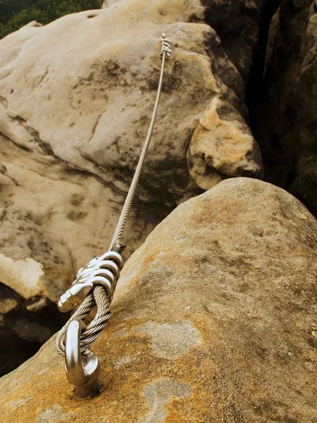 Detail of steel anchor eye and rope end anchored into sandstone rock. Iron twisted rope fixed in block by screws snap hooks. — Stock Photo, Image