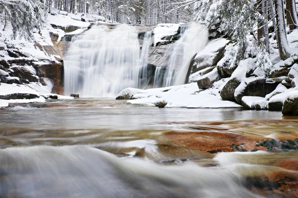 Winter view over snowy boulders to cascade of waterfall. Wavy water level.. Stream in deep freeze. — Stock Photo, Image