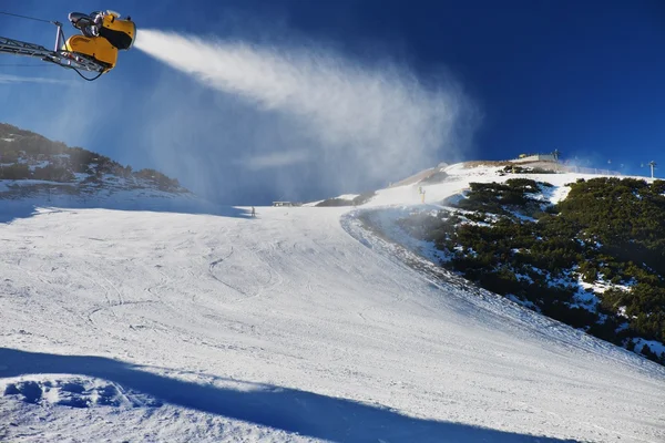 Snow making on slope. Skier near a snow cannon making fresh powder snow. Mountain ski resort and winter calm mountain landscape.