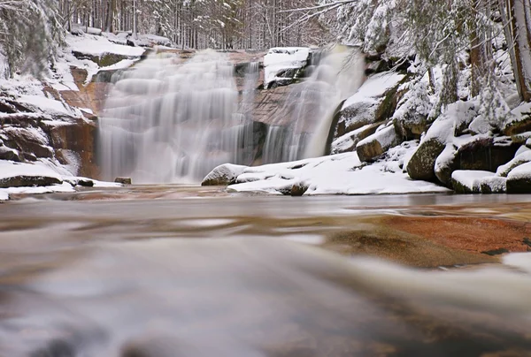 Winter view over snowy boulders to cascade of waterfall. Wavy water level.. Stream in deep freeze. — Stock Photo, Image