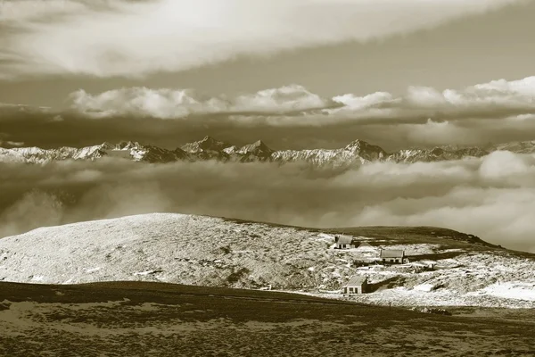 Cabanas em picos de Alpes colina, montanhas rochosas afiadas no horizonte. Dia de inverno ensolarado. Haste congelada de grama em grande prado de montanha . — Fotografia de Stock