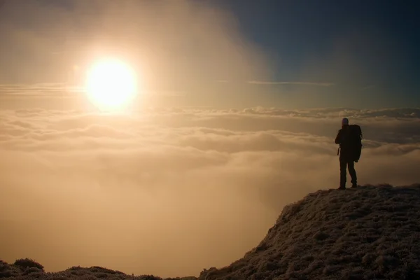 Turista con grande zaino è in piedi sul punto di vista e guardando nella valle nebbiosa. Sunny mattina d'inverno . — Foto Stock