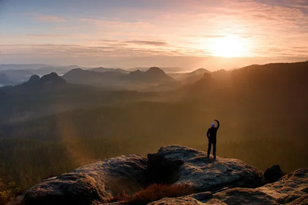 Turista scatta foto con smart phone sulla vetta della roccia. Paesaggio nebbioso da sogno, primavera arancio rosa foschia alba in una bellissima valle sotto le montagne rocciose . — Foto Stock