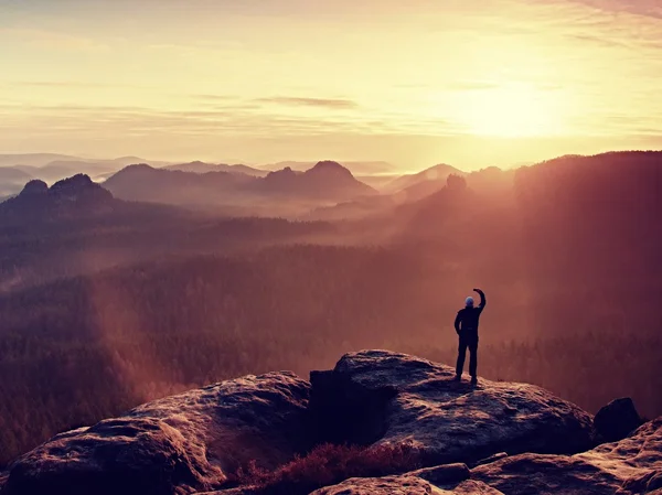 L'uomo scatta foto con smart phone sulla vetta dell'impero rock. Paesaggio nebbioso da sogno, primavera arancio rosa nebbia alba in una splendida valle del parco della Sassonia Svizzera . — Foto Stock