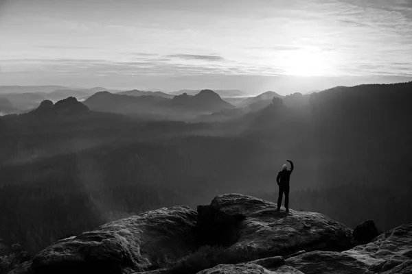 Man takes photos with smart phone on peak of rock empire. Dreamy fogy landscape, spring orange pink mist — Stock Photo, Image