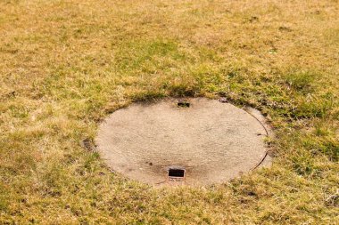 Beton menhol kapağı drenaj sistemi kırpılmış kuru ot ortasında