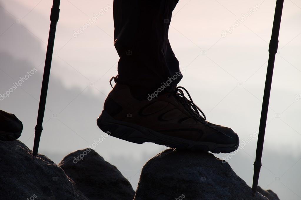 Man hiker legs  and poles stand on mountain peak rock