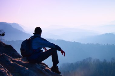 Turizm spor sırt çantası ile oturup kayalık tepe ve puslu Vadisi feryat izlerken. Güneşli sisli gün doğumuna rocky Dağları.