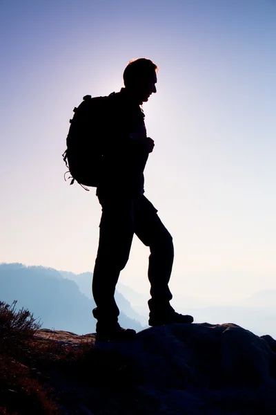 Touriste avec sac à dos sportif se tenir sur le point de vue rocheux et regarder dans le soufflet vallée brumeuse. Coucher du jour ensoleillé et brumeux dans les montagnes rocheuses . — Photo